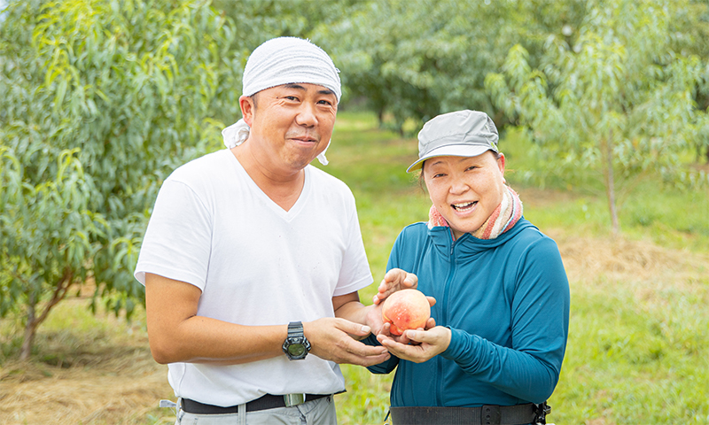 写真：末房さん夫妻が桃を持ち微笑んでいる様子2